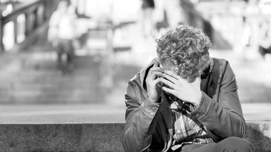 En ung man som sitter och pratar i mobiltelefon med en hand framför ansiktet.