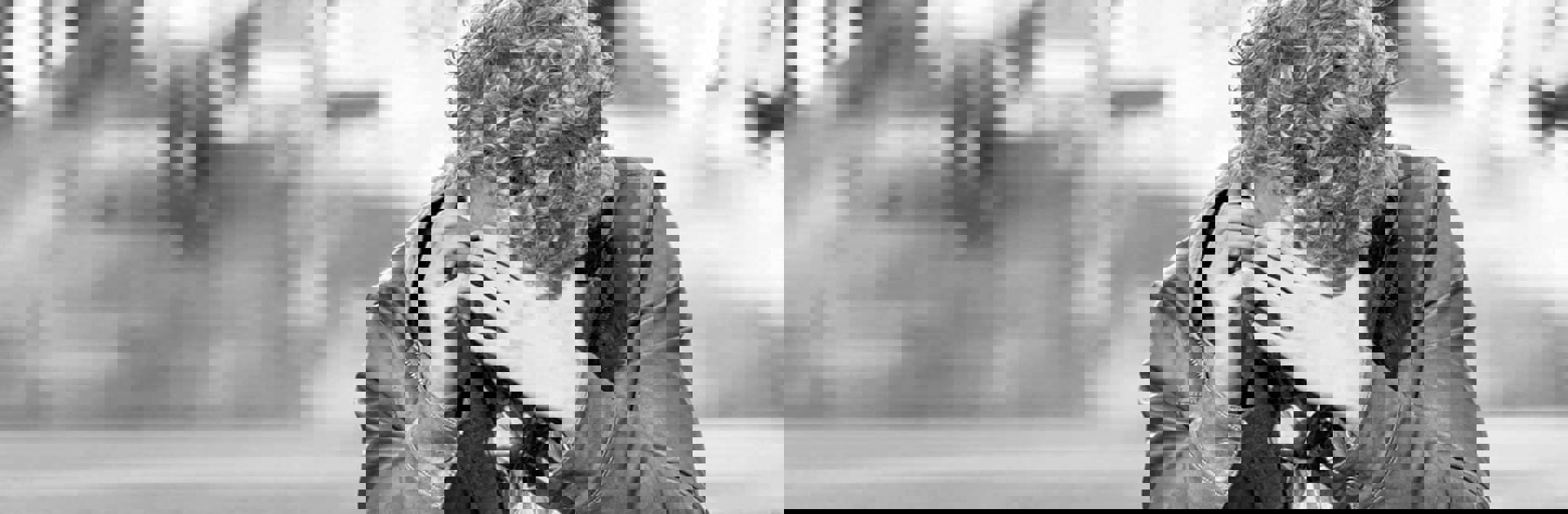 Svartvit bild på en ung man sitter och pratar i mobiltelefon med en hand framför ansiktet.